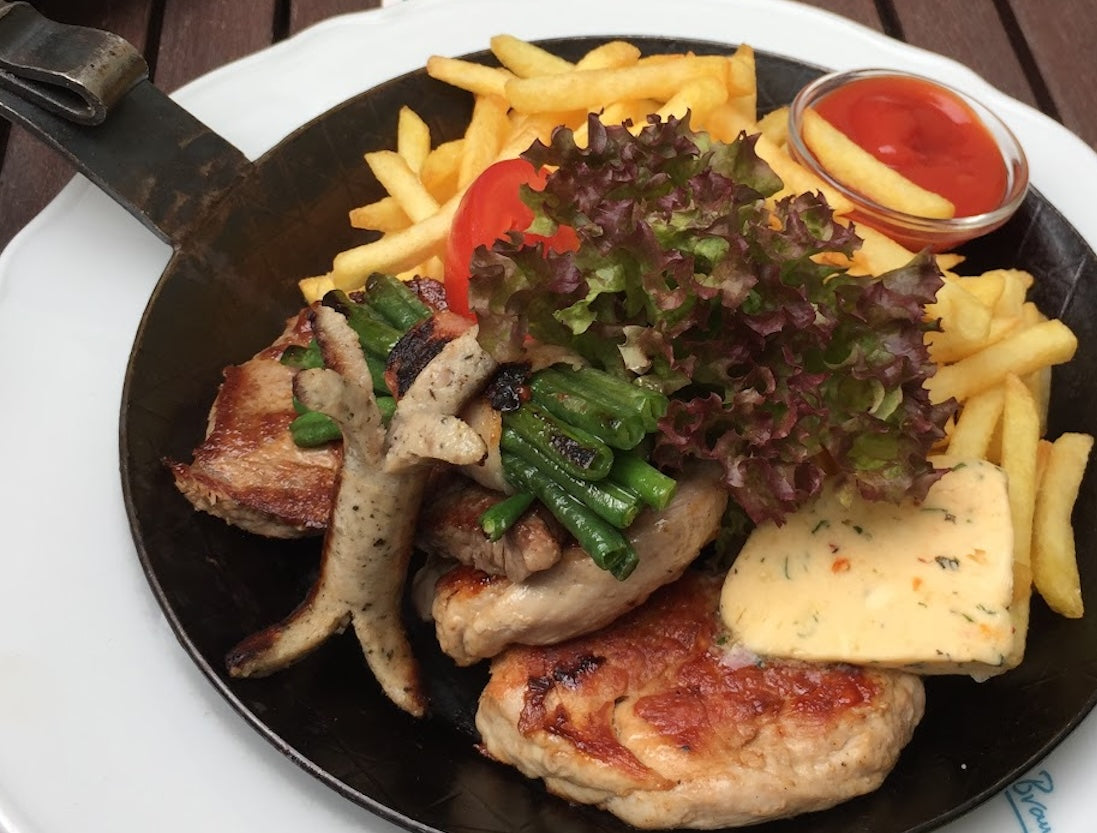 Traditional Bavarian meal with grilled pork, bratwurst, fries, and salad served in a skillet at Bischofshof am Dom in Regensburg, Germany.