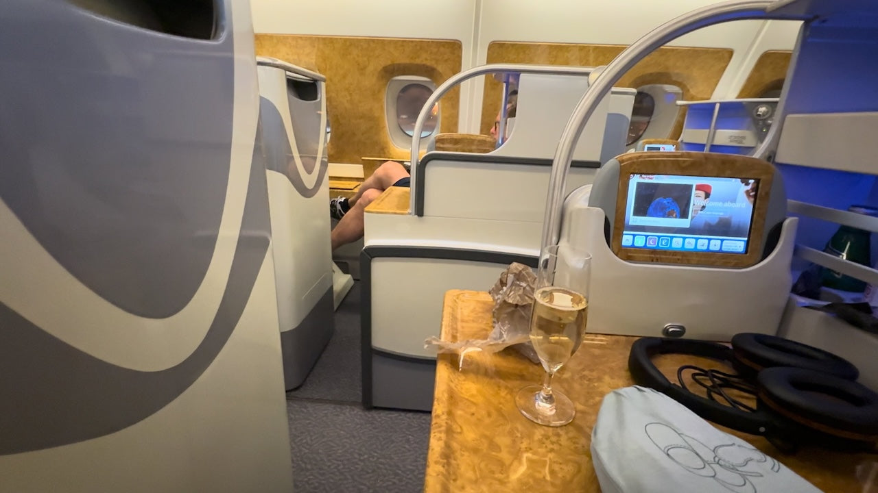 Emirates A380 Business Class cabin with woodgrain finishes, screen, and champagne
