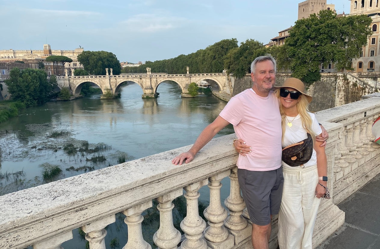 Couple standing on bridge in Rome with Ponte Sant’Angelo in the background