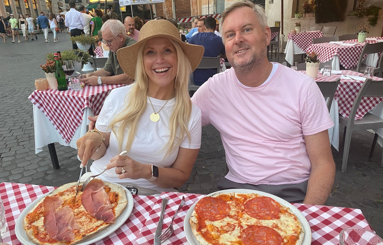 Gen X couple dining outdoors in Rome with wood-fired pizzas on a cobblestone street