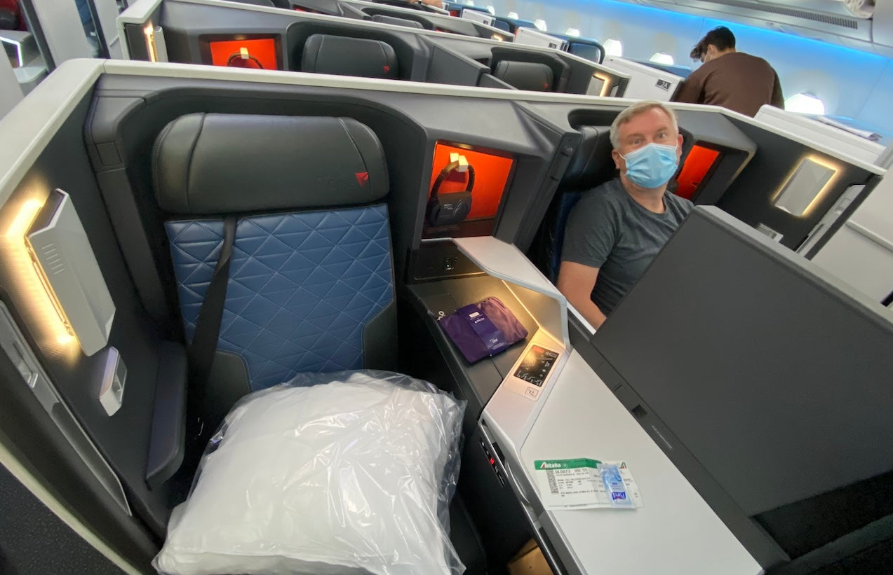 Passenger seated in Delta One Suite aboard a Delta Air Lines flight, featuring a fully lie-flat seat, personal entertainment screen, and amenities for a premium long-haul experience.