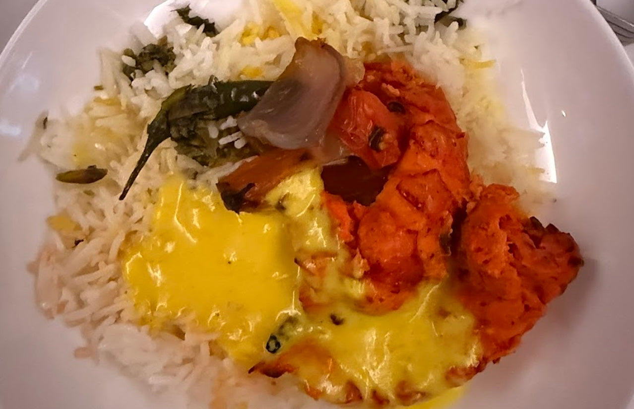 Plate of in-flight Indian cuisine featuring tandoori chicken, saffron rice, and roasted vegetables served aboard a premium international flight.