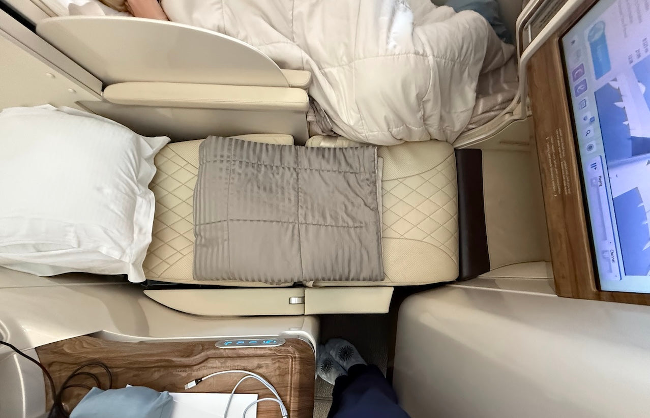Overhead view of a Business Class seat fully extended into a lie-flat bed with a pillow, comforter, and blanket arranged neatly, showing the luxury sleep setup.